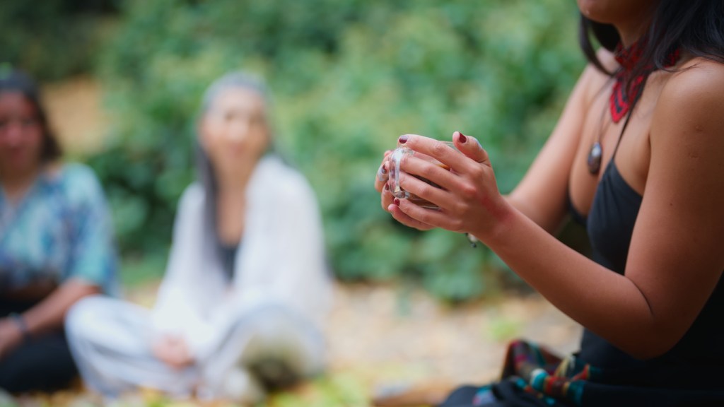 A woman in a black dress is serving cacao drinks during a cacao ceremony in nature. A cacao ceremony is a spiritual ritual for cleaning soul, connecting with the nature, healing, mental wellbeing, mindfulness and self-exploration. People who join the ceremony consume ceremonial cacao.